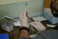 Person with gloves draws liquid from vial with syringe