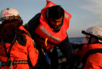 MSF search and rescue teams helping a survivor get onto the rescue boat.