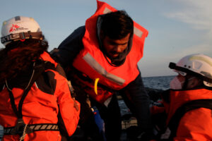 MSF search and rescue teams helping a survivor get onto the rescue boat.