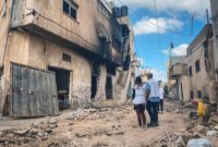 2 MSF team members standing in front of a burnt house surrounded by damaged houses in Jenin.
