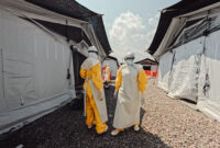 Staff members dressed in full PPE, standing next to white tents.
