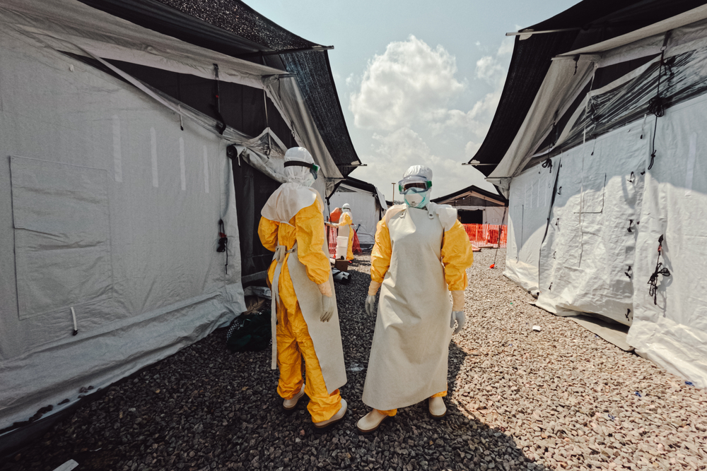 Staff members dressed in full PPE, standing next to white tents.